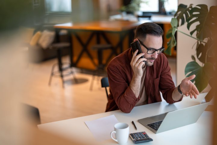 Man sitter vid dator och pratar i telefon