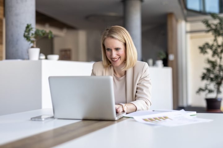 En glad kvinna som arbetar vid sin laptop, vilket förmedlar innovation och entusiasm i en modern kontorsmiljö fylld av positivitet.