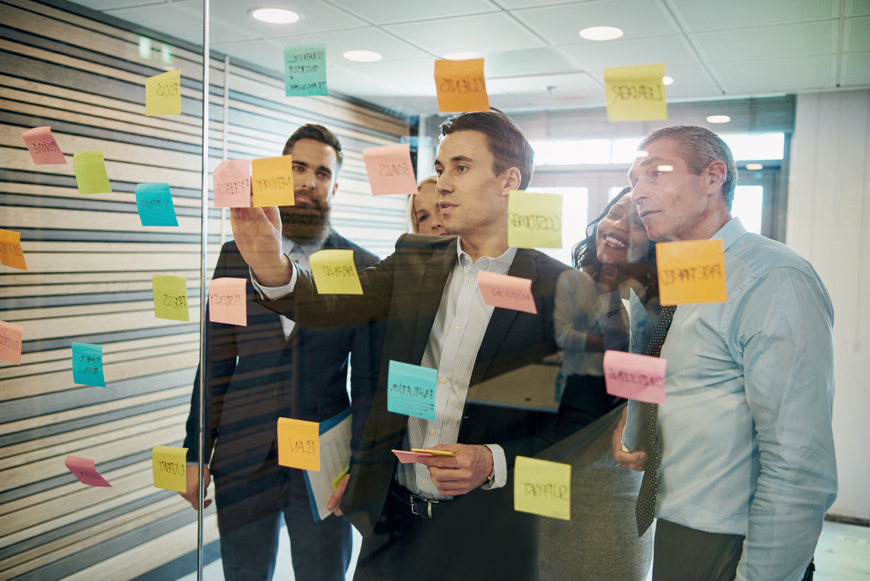 Grupp av affärspersoner som brainstormar med post-it-lappar på ett glasfönster.