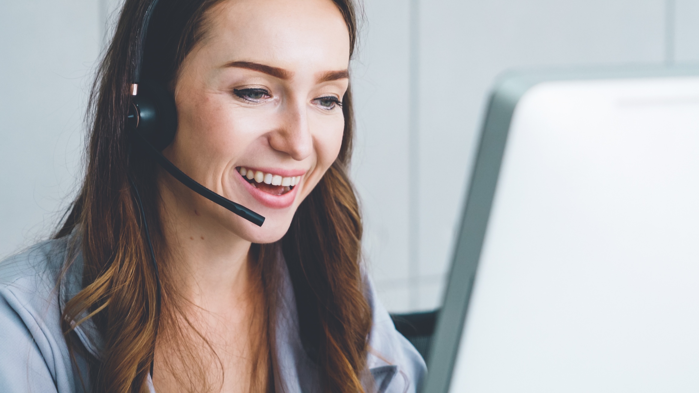 Kvinna sitter och pratar i headset vid dator
